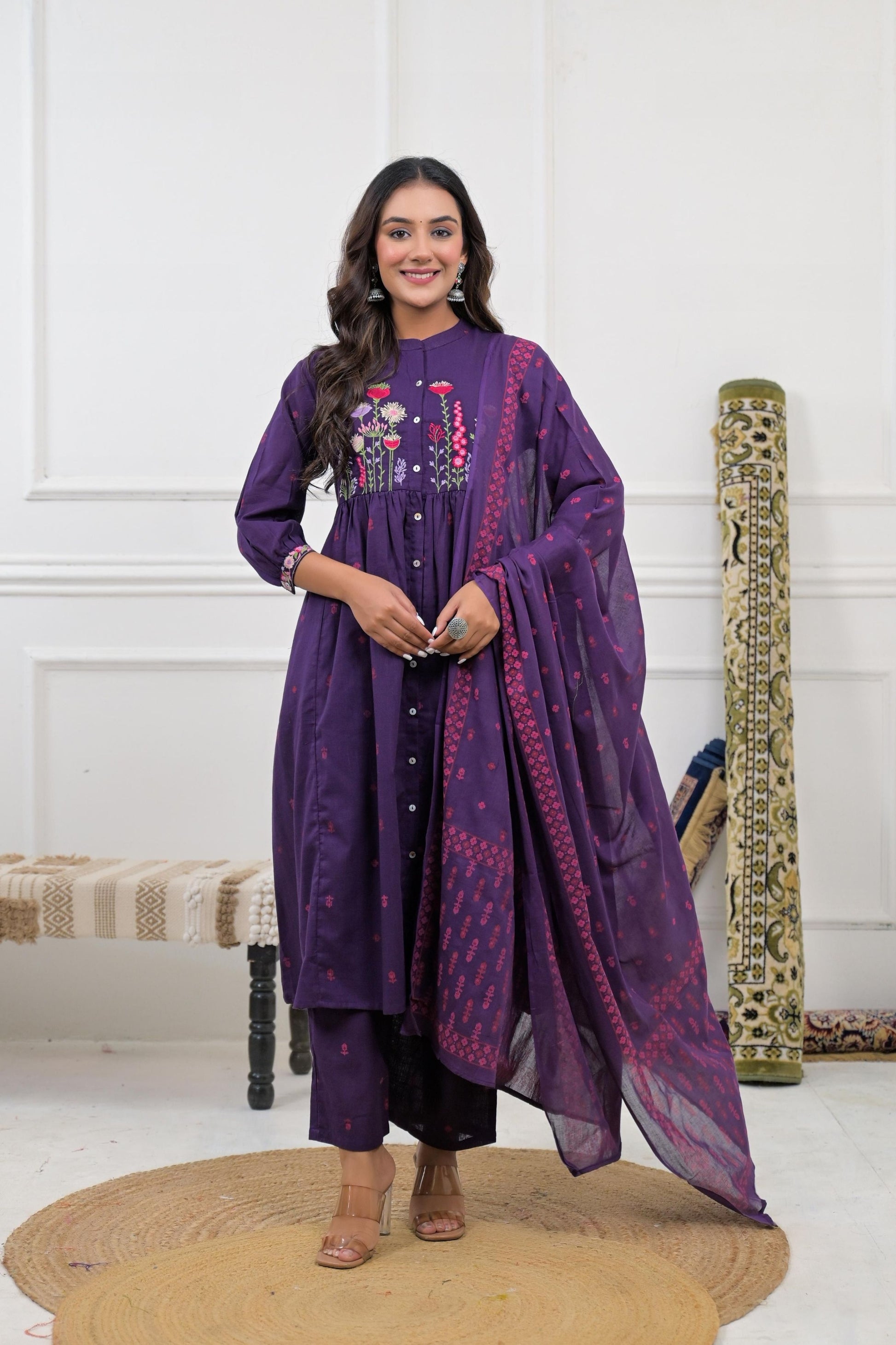 A woman wears a floral embroidered kurta set with a dupatta, featuring intricate white embroidery on a cream fabric.